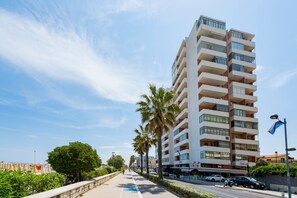 A multi-story building with balconies, a clear sky, and a sidewalk with palm trees. - GuestHost - Sea View Moro Apartment (Montesilvano)
