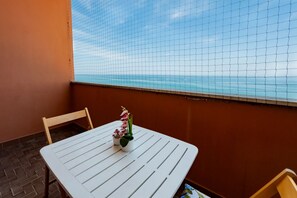 A white table with a potted plant, a chair, and a view of the ocean through a wire mesh. - GuestHost - Sea View Moro Apartment (Montesilvano)