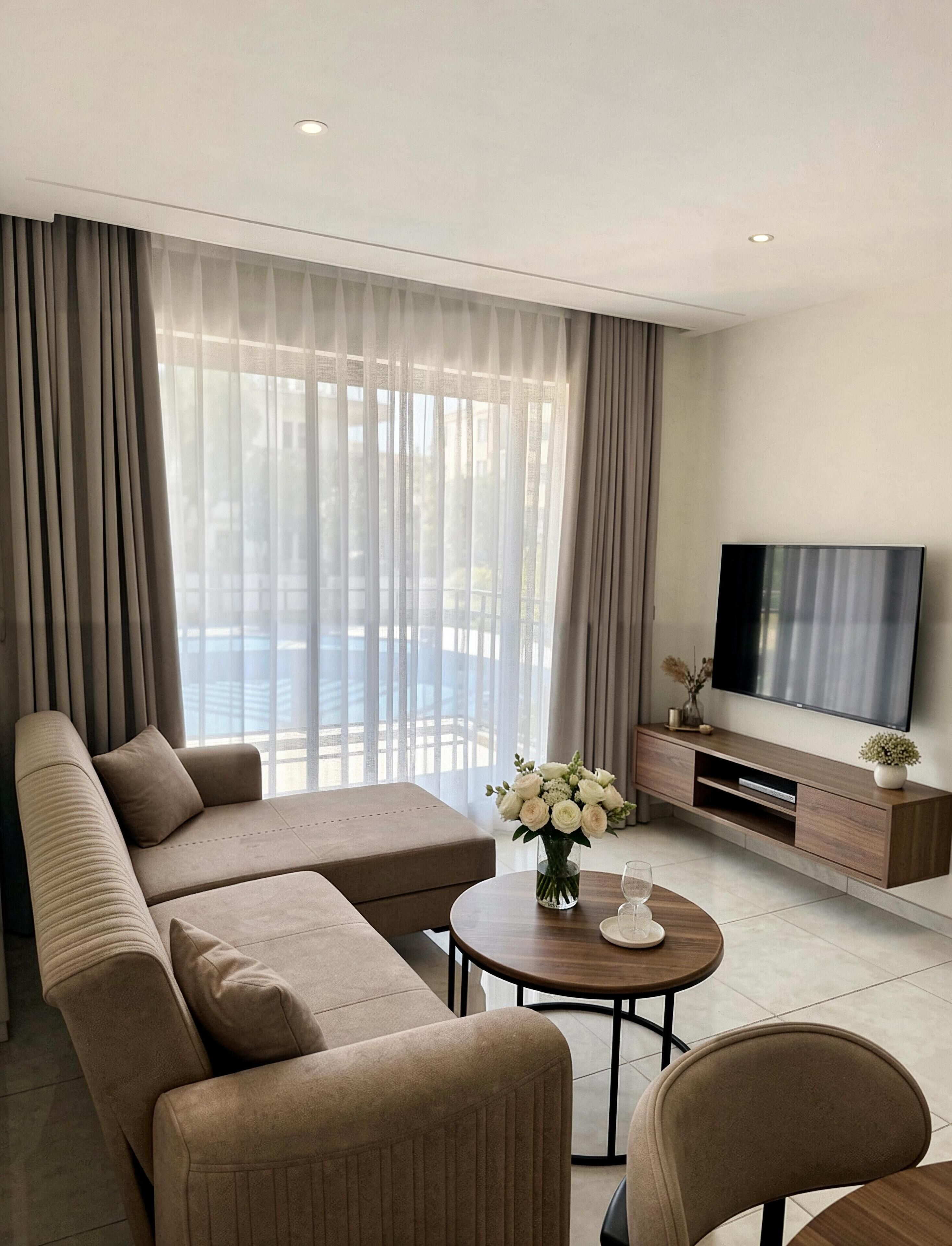 Ein modernes Wohnzimmer mit einer Couch, einem Couchtisch, einem Fernseher und Blick durch große Fenster.