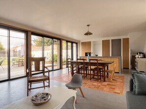 A modern kitchen with wooden cabinets, a dining area with a table and chairs, and large sliding glass doors leading to an outdoor patio. - Charming home – Large garden – Perfect for families (Pornichet)