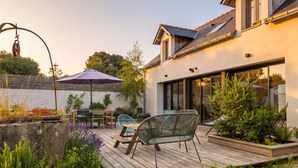 Una casa moderna con terraza de madera, mobiliario exterior y jardín.