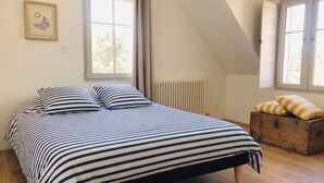 Un dormitorio con cama, dos ventanas, un radiador y un aparador de madera.