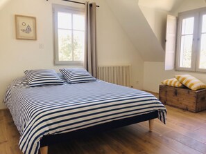 A bedroom with a bed, two windows, a radiator, and a wooden chest of drawers. - Charming home – Large garden – Perfect for families (Pornichet)