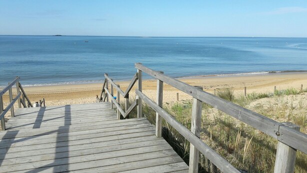 Un paseo marítimo de madera que conduce a una playa con cielos despejados y aguas tranquilas.