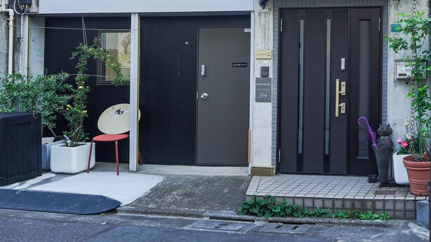 Un edificio de dos pisos con una puerta negra, un balcón pequeño y una planta en maceta.