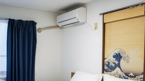 Habitación de hotel con cama, equipo de aire acondicionado y una pintura de una ola japonesa en la pared.