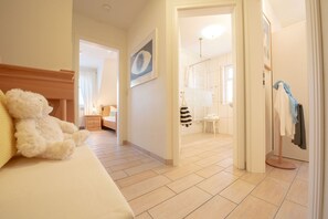 Ein Hotelzimmer mit Bett, einem Teddybären, einem Gemälde, einem Badezimmer inklusive Handtuchhalter und einem Kleiderständer.