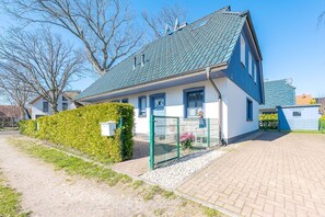 Ein zweistöckiges Haus mit befestigter Auffahrt, grünem Zaun und einer Hecke.