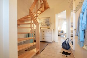 Eine Holztreppe führt zu einem Wohnbereich mit einem weißen Schminktisch, einer blauen Tasche und einem Paar Schuhen auf dem Boden.