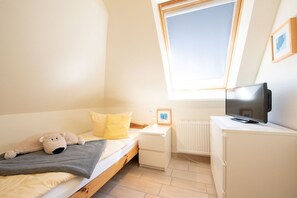 Ein Schlafzimmer mit einem Bett, einem Fernseher, einem kleinen Nachttisch, einem Heizkörper und einem Fenster.