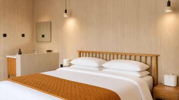 Habitación de hotel con una cama de cabecera de madera, una mesita de noche con lámpara, un espejo y otra mesita más pequeña con un dispositivo.