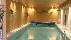 An indoor swimming pool with wooden walls, a tiled floor, and a seating area with chairs. - Hotell Cikada (Mariehamn)