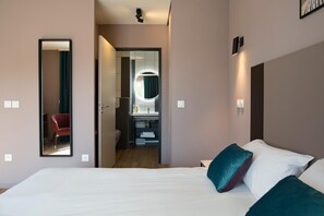 Ett hotellrum med en säng, en spegel, ett badrum med en rund spegel och en röd stol.
