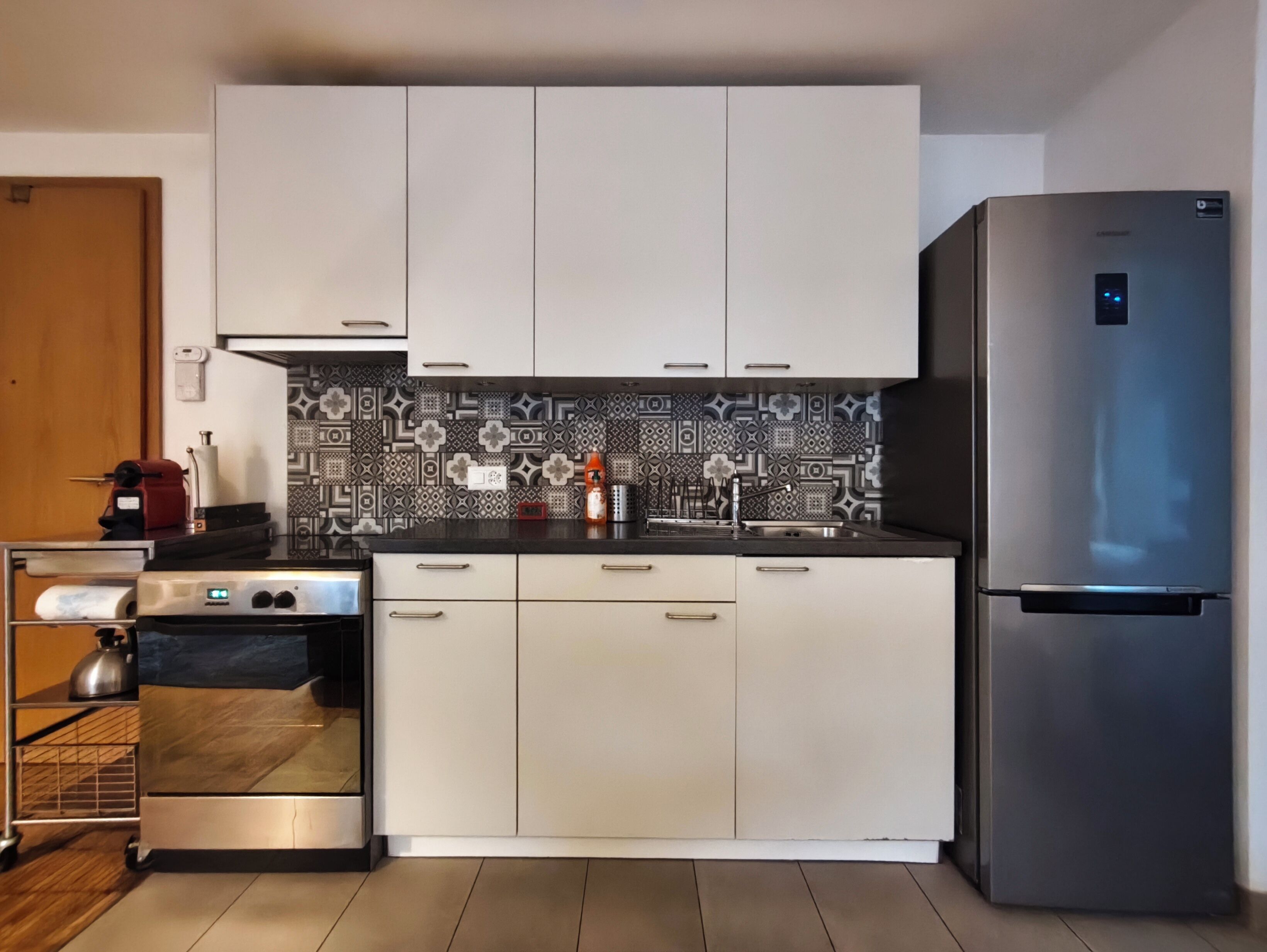A modern kitchen with white cabinets, a stainless steel refrigerator, and patterned backsplash tiles.
