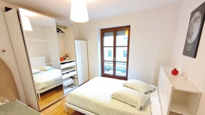 Ein Schlafzimmer mit Bett, Kleiderschrank, Fenster und einem kleinen Tisch mit einer Granatapfel.