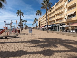 Una playa con palmeras, un parque infantil y un edificio con terraza.