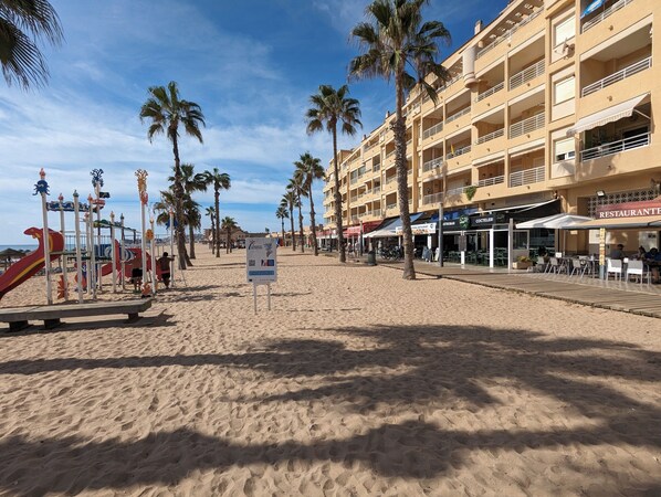 Una playa con palmeras, un parque infantil y un edificio con terraza.