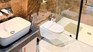 Um banheiro moderno com parede de mármore, box de vidro, pia branca e vaso sanitário.