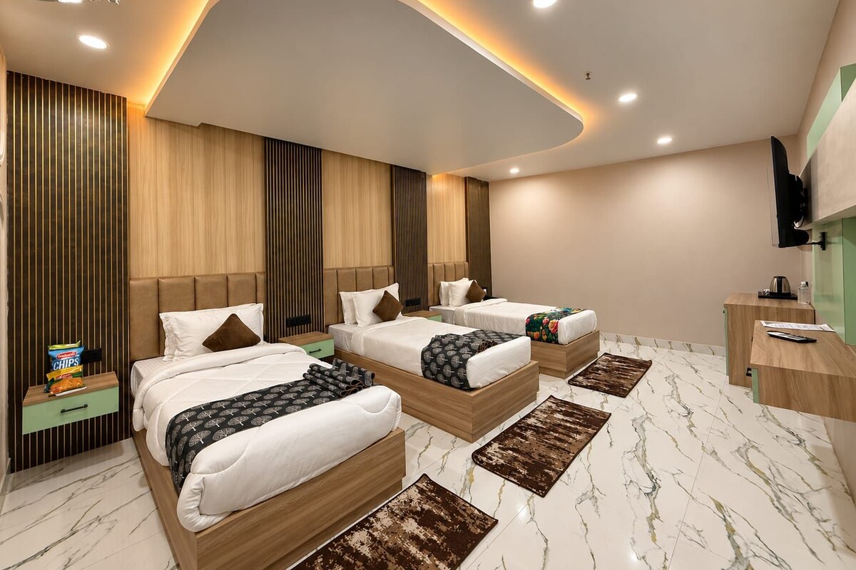 A modern hotel room with three beds, a desk, and a television.