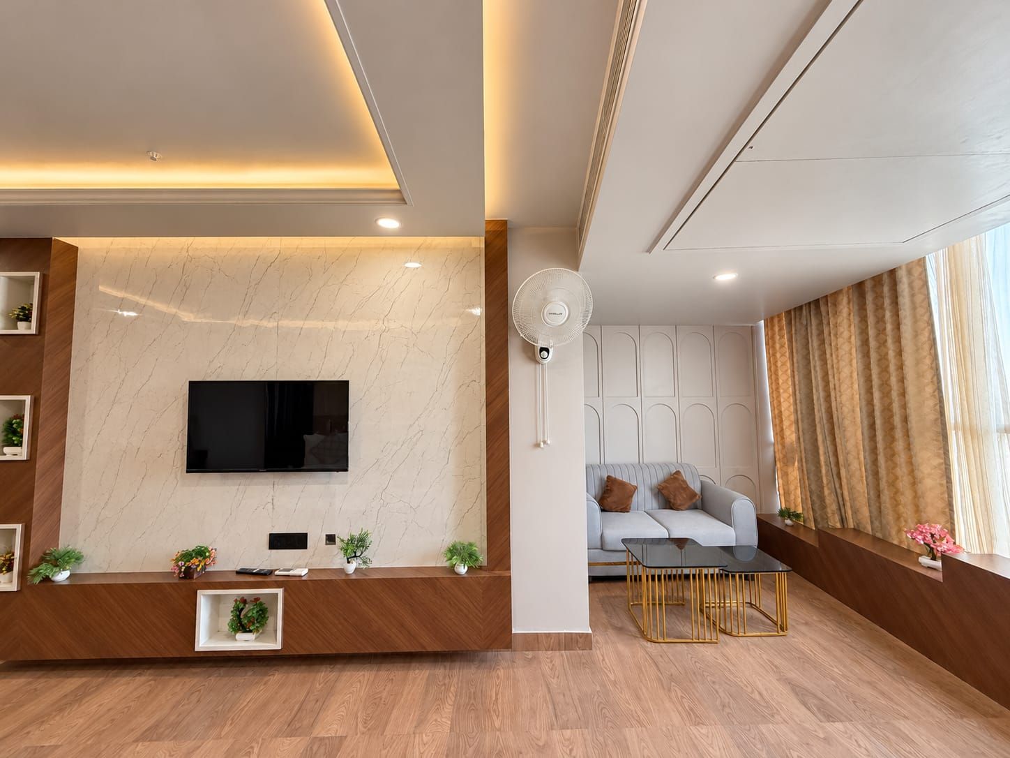 A modern living room with a flat-screen TV, a wooden reception desk, a sofa, and a coffee table.