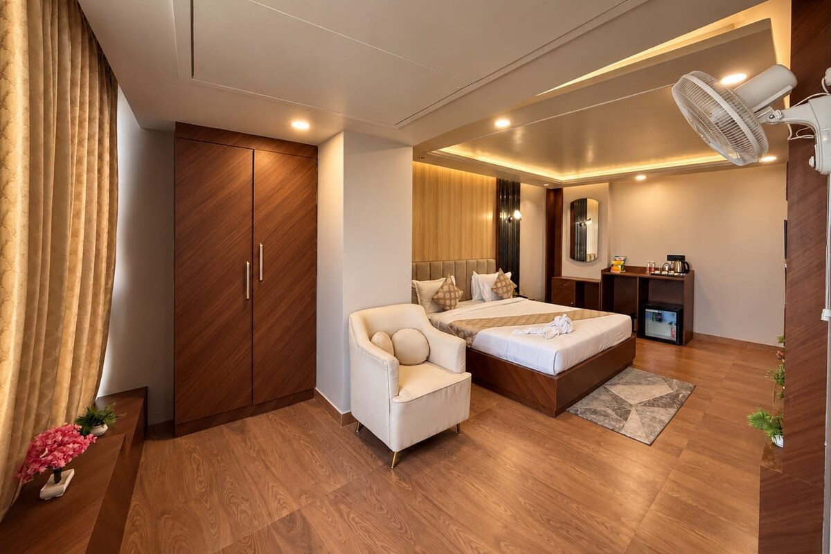 A modern hotel room with a bed, a seating area, a wardrobe, and a small kitchenette.