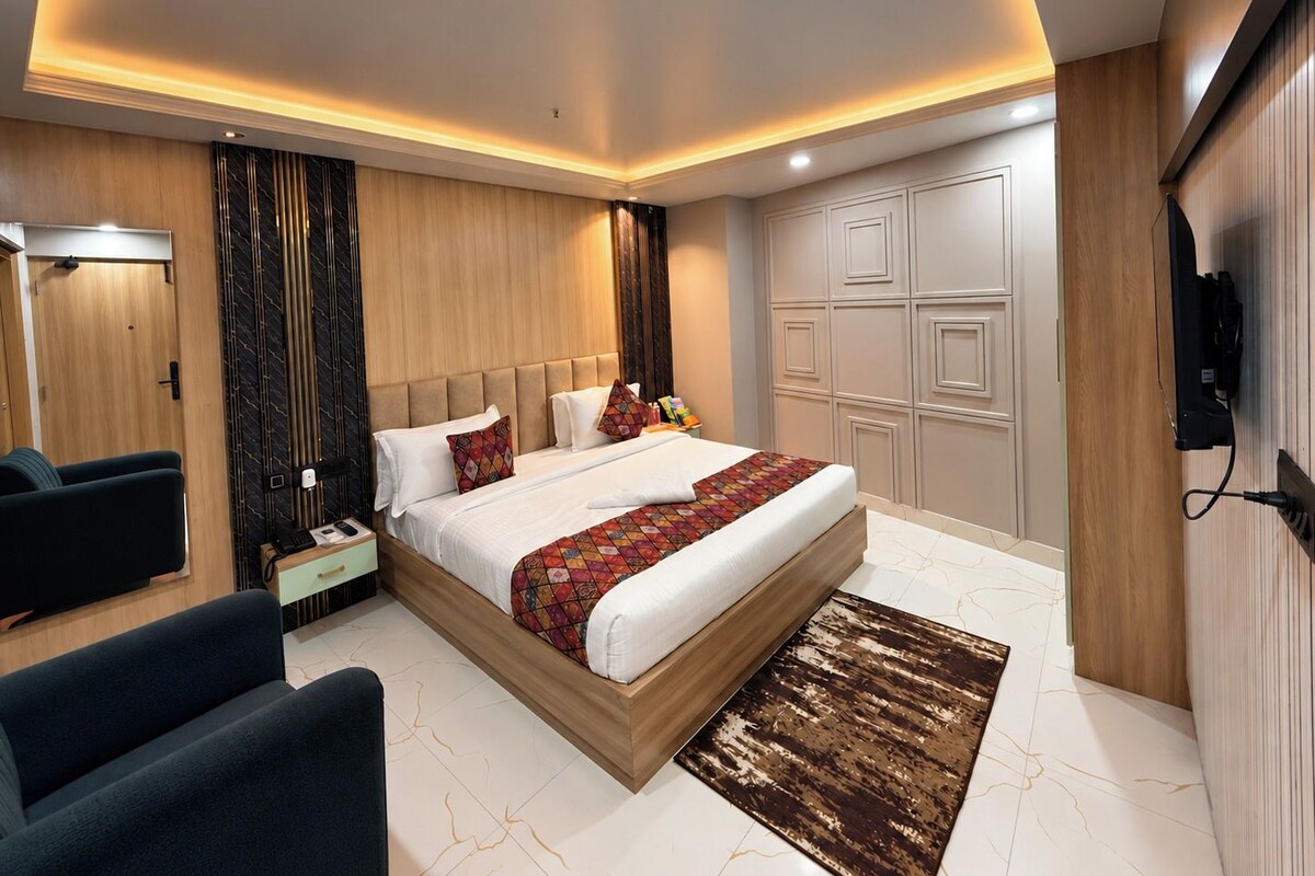 A modern hotel room with a large bed, a bedside table, a chair, a TV, and a wardrobe.