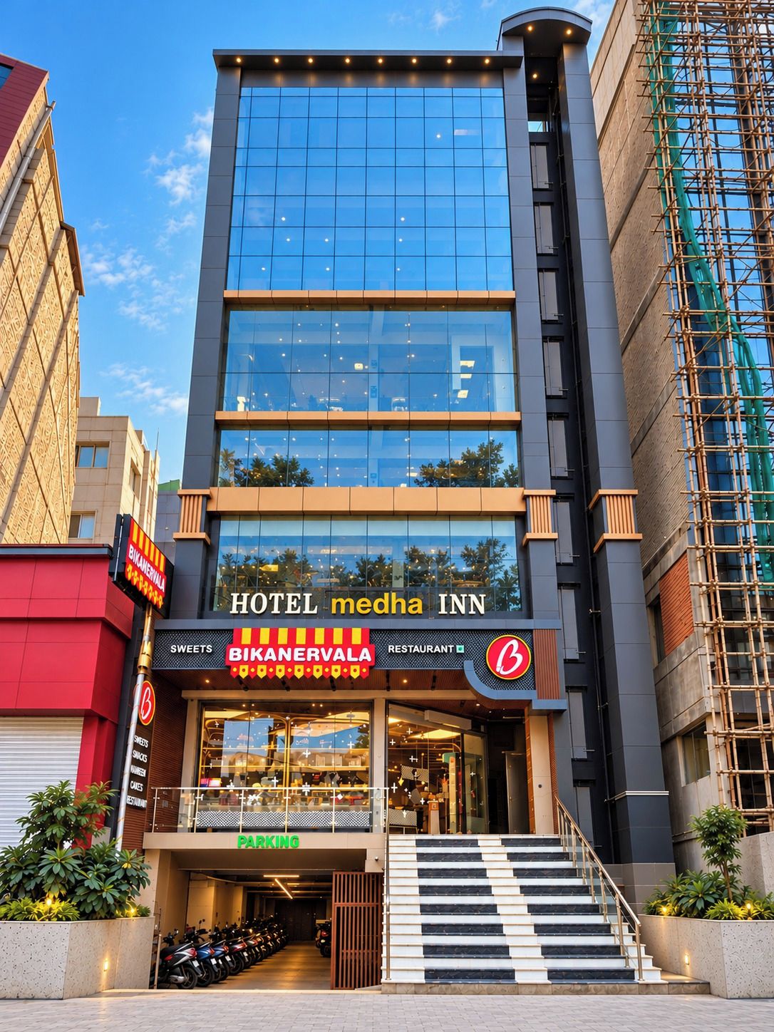 A multi-story hotel with a glass facade, a restaurant named Bikanarvala, and a parking area with motorcycles.