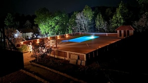 A swimming pool surrounded by a fence, with trees and a small building in the background.