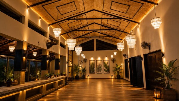 A spacious lobby with a high ceiling, chandeliers, potted plants, and artwork on the walls.