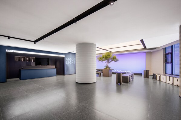 A modern hotel lobby with a reception desk, a large white column, and a seating area with a potted plant. - Chongqing Jiefangbei Jiaochangkou qingju (Chongqing)
