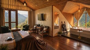 Quarto com cama, área de estar, televisão e vista para as montanhas.