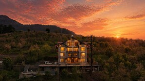 Uma casa com vários andares e varanda, cercada por árvores e colinas.