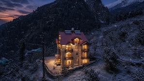 A multi-story log cabin with a red roof, surrounded by snow-covered trees and mountains. - AKIRA BY SKYLORE (Manali)
