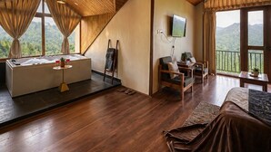 Um quarto espaçoso com teto de madeira, uma janela grande com cortinas, banheira, sofá, escrivaninha e televisão.