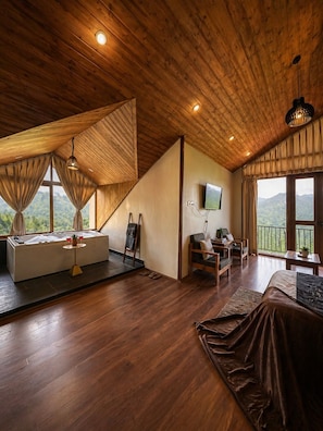A spacious room with a wooden ceiling, a large window with curtains, a bathtub, a sofa, a desk, and a TV. - AKIRA BY SKYLORE (Manali)
