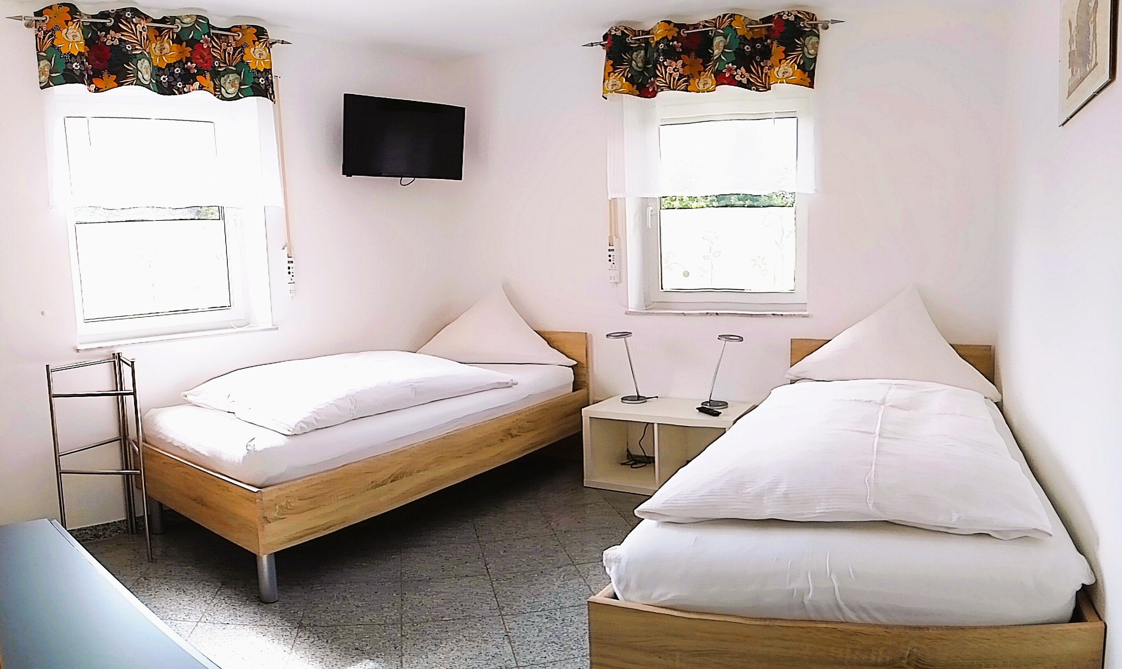 A bedroom with two single beds, a TV on the wall, and a window with a curtain.