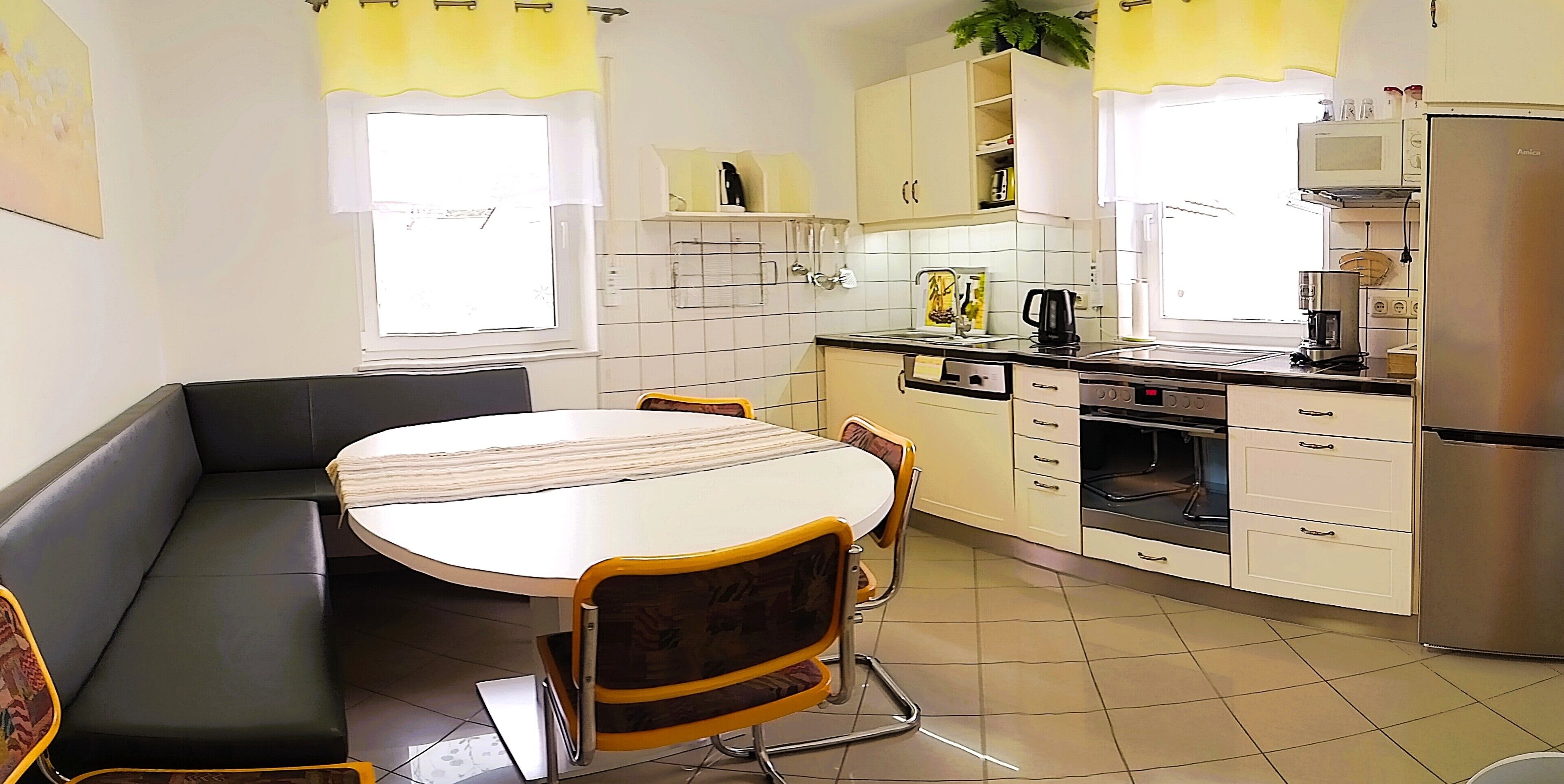 A compact kitchen with a dining table, chairs, a built-in oven, and a refrigerator.