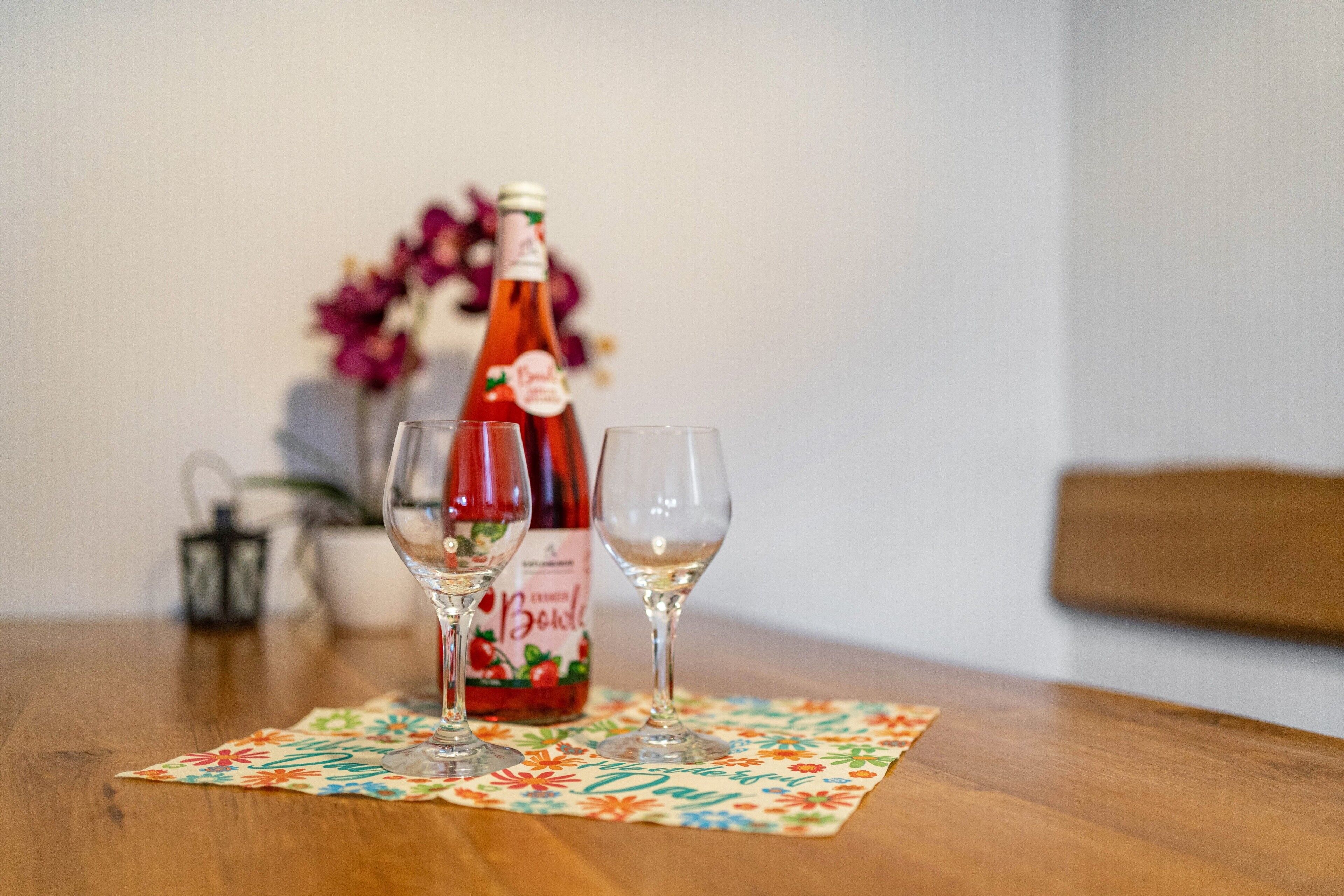 Une table avec une bouteille de boisson et deux verres, le tout posé sur un set de table à motifs floraux.