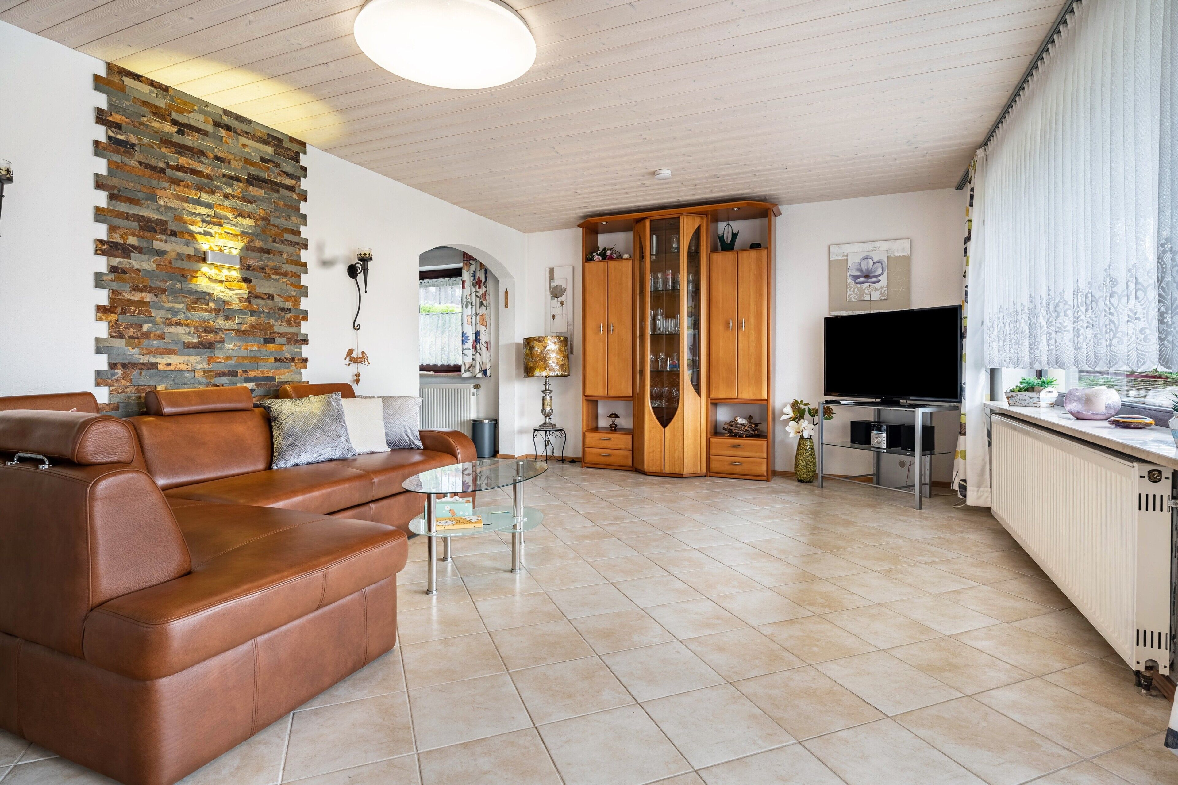 Ein Wohnzimmer mit einem braunen Ledersofa, einem Glastisch, einem Holzschrank und einem Fernseher.