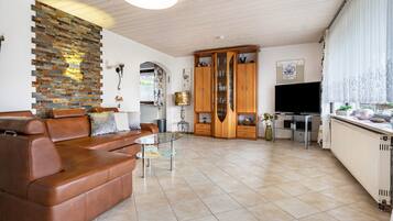 Ein Wohnzimmer mit einem braunen Ledersofa, einem Glastisch, einem Holzschrank und einem Fernseher.