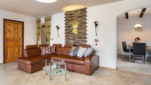 A living room with a brown leather sofa, a glass coffee table, a stone wall, and a wooden door. - Apartment 'Spatzennest' with Mountain View, Private Terrace and Wi-Fi (Arrach)