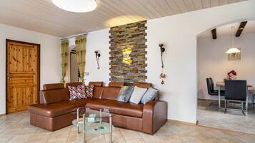 Ein Wohnzimmer mit braunem Ledersofa, einem Glastisch, einer Steinwand und einer Holztür.