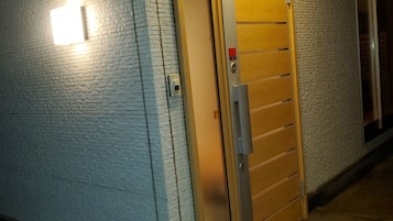 Een gevel met een structuur, een houten deur met een metalen handgreep, en een lamp aan de muur.