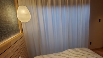 Een slaapkamer met een bed, gordijnen, een hanglamp en houten lambrisering.