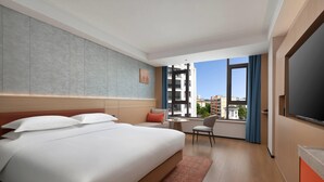 Habitación de hotel con una cama grande, un escritorio, una silla, un televisor y una ventana con vista a edificios.