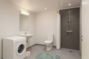 A modern bathroom with a washing machine, toilet, sink, and shower. - Bright Modern Apartment in City Center (Aalborg)