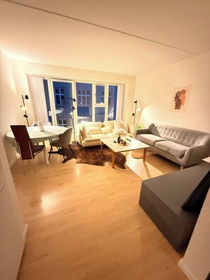 A living room with a sofa, a coffee table, and a dining area with a table and chairs. - Bright Modern Apartment in City Center (Aalborg)