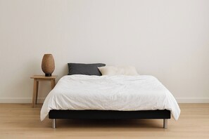 Ein Bett mit weißer Daunendecke, einem dunklen Kopfteil und einem kleinen Nachttisch mit einem gewobenen Korb.