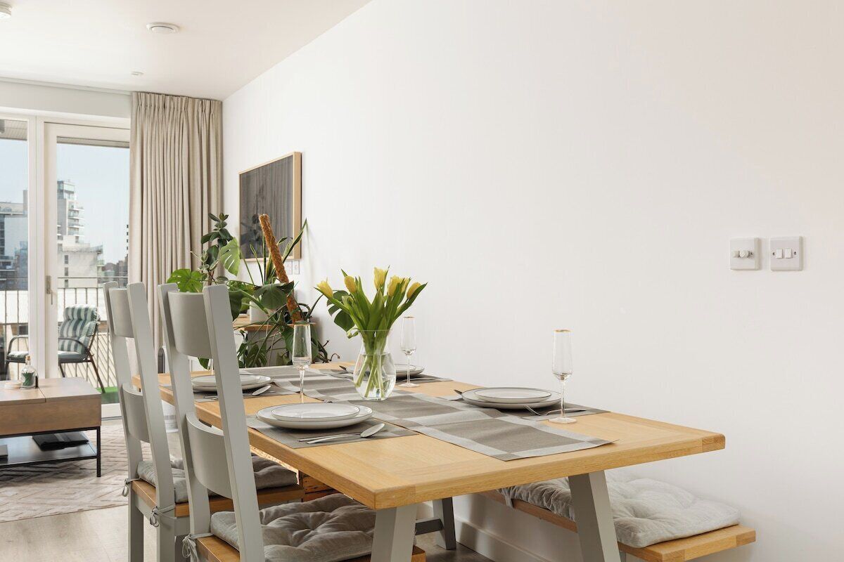 A modern dining area with a wooden table, white chairs, and a vase of flowers.