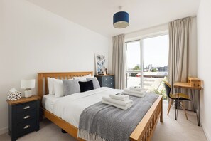 Ein Schlafzimmer mit Bett, Nachttischen, einem Schreibtisch und Blick auf die Stadt.